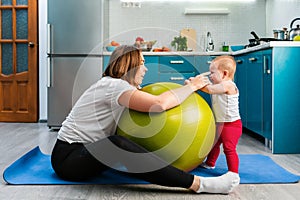 Yoga at home. A young mother leaning on a fit ball, funny communicates with her baby. The concept of fitness with children at home