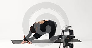 A yoga instructor conducts an online lesson and records a video, performing the Ardha Hanumanasana exercise