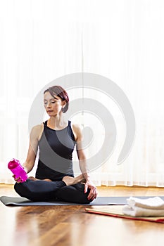 Yoga Lifestyle Concepts. Tranquil Caucasian Woman in Yoga Pose Indoors. Posing In Front of Big Window With Stack of White Towels