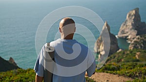 Yoga man walking edge cliff holding mat. Focused sportsman looking ocean coast
