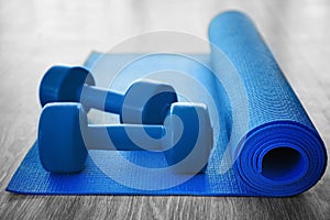 Yoga mat with dumbbells on wooden floor