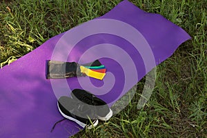 Yoga mat, elastic expanders and sneakers on grass background.