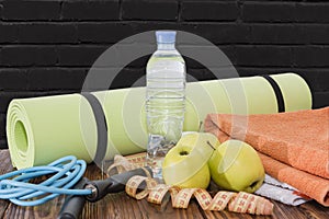 Yoga Mat and water bottle close-up. Sports equipment, three green apples and a jump rope.