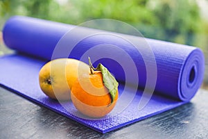 Yoga mat, water, orange and mango on a wooden background. Equipment for yoga. Concept healthy lifestyle, diet and sport. Copy spac