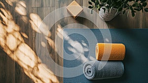 Yoga mat on a wooden floor with two rolled towels, one yellow and one gray photo