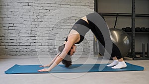 Yoga mat young athletic woman stretching hip, hamstring muscles, leg muscles indoors in a gym. Stretching exercises