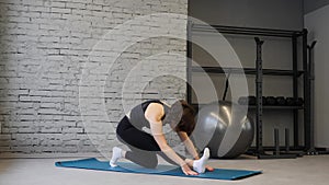 Yoga mat young athletic woman stretching hip, hamstring muscles, leg muscles indoors in a gym. Stretching exercises