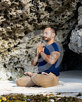 Yoga meditation on the beach. Asian man sitting on sand in Lotus pose. Padmasana. Hands in namaste mudra. Closed eyes. Yoga