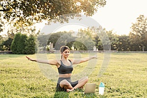 Yoga meditation online with laptop on the grass in green park. Fit girl training outdoor. Relaxation and meditating.