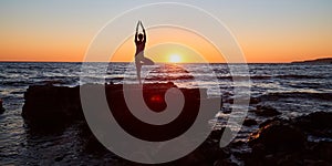 Yoga meditation. Pilates and active lifestyle concept. Fit female standing in yoga position. Sunset over sea landscape.