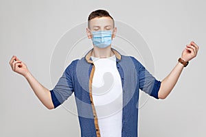 Yoga and meditation. Portrait of calm serious young man in casual style with surgical medical mask standing in yoga pose and