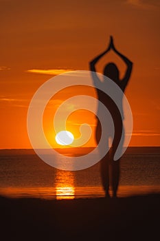 yoga meditation, silhouette of woman at sunset in pose tree with outstretched arms.