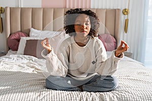 Yoga mindfulness meditation. Young healthy African girl practicing yoga at home. Woman sitting in lotus pose on bed