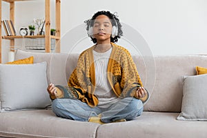 Yoga mindfulness meditation. Young healthy african girl practicing yoga at home. Woman sitting in lotus pose on couch