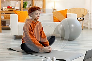Yoga mindfulness meditation. Young healthy african girl practicing yoga at home. Woman sitting in lotus pose on yoga mat