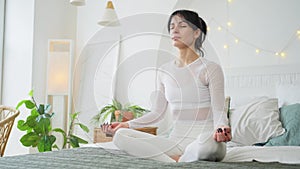 Yoga mindfulness meditation. Young healthy woman practicing yoga in bedroom at home. Woman sitting in lotus pose on bed