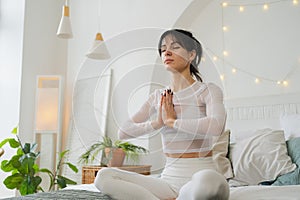 Yoga mindfulness meditation. Young healthy woman practicing yoga in bedroom at home. Woman sitting in lotus pose on bed