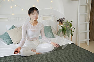 Yoga mindfulness meditation. Young healthy woman practicing yoga in bedroom at home. Woman sitting in lotus pose on bed