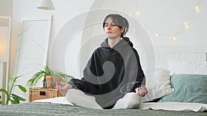 Yoga mindfulness meditation. Young healthy woman practicing yoga in bedroom at home. Woman sitting in lotus pose on bed