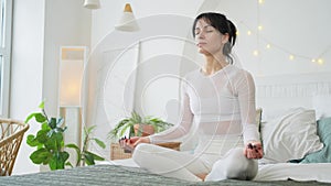 Yoga mindfulness meditation. Young healthy woman practicing yoga in bedroom at home. Woman sitting in lotus pose on bed