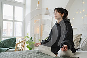 Yoga mindfulness meditation. Young healthy woman practicing yoga in bedroom at home. Woman sitting in lotus pose on bed