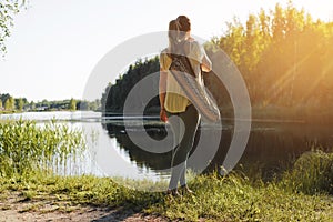 Yoga in nature outdoors. Young fitness woman standing by the lake with yoga mats, back view.