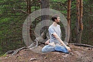 Yoga in nature, young caucasian man sit in lotus pose in meditation outdoors in pine forest and doing yoga exercises, copy space