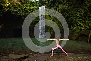 Yoga near waterfall. Young woman practicing Virabhadrasana II, Warrior II Pose. Standing asana. View from back. Healthy lifestyle