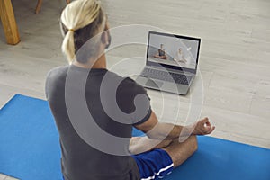 Yoga online home. Young man following online yoga class and doing his morning meditation or breathing exercises on mat