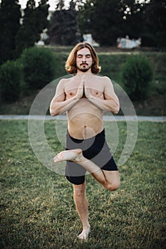 Yoga at park. Bearded man doing yoga in the green park.