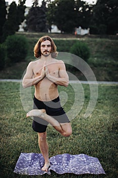 Yoga at park. Bearded man doing yoga in the green park.