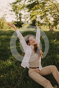 Yoga at park with sunlight. Young woman reaches and sitting on green grass. Concept of calm and meditation