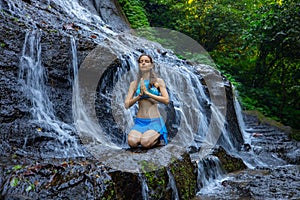 Yoga pose. Young Caucasian woman meditating, practicing yoga at waterfall. Vajrasana or Diamond pose. Hands in namaste mudra. Goa
