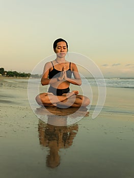 Yoga practice on the beach. Lotus pose. Padmasana. Hands in namaste mudra. Closed eyes. Meditation and concentration. Zen life.