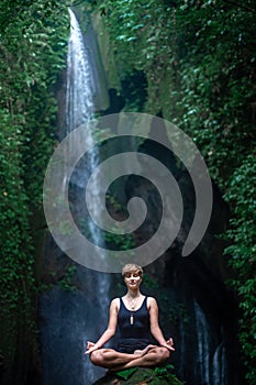 Yoga practice and meditation in nature. Woman practice near waterfall.