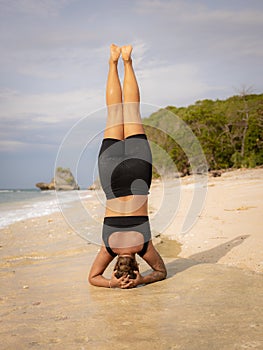 Yoga practice near the ocean. Caucasian woman practicing Salamba Shirshasana, Yoga Headstand is an inverted asana. Balancing asana