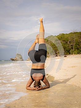 Yoga practice near the ocean. Caucasian woman practicing Salamba Shirshasana, Yoga Headstand is an inverted asana. Balancing asana