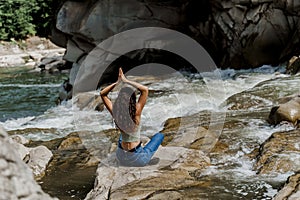 Yoga on the rocks near waterfall in mountain river. Girl is travelling in Karpathian mountains. Cascade waterfall and
