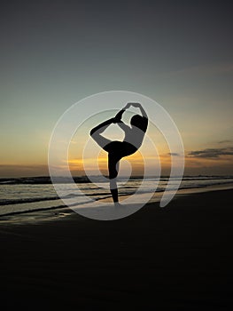Yoga silhouette. Sunset beach yoga. Slim woman practicing standing asana Natarajasana, Lord of the Dance Pose. Balancing, back