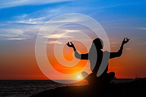 Yoga silhouette of woman meditating on the ocean beach.