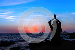 Yoga silhouette of woman meditating on the ocean beach