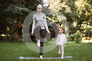 Muslim mother and her daughter, having workout in the park, doing high stepping exercise photo