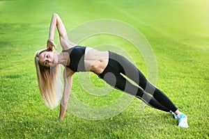 Yoga or stretching on the lawn. A young girl in a black tracksuit. The concept of a healthy lifestyle. Copy of the space