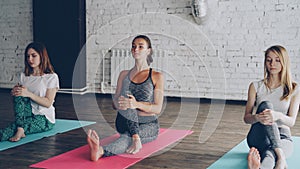 Yoga students are sitting on mats and doing twist yoga pose then stretching leg, losing balance and laughing together