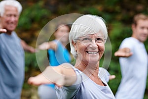Yoga takes me to my happy place. Shot of a senior woman doing yoga with other people outdoors.