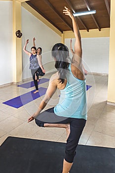 Yoga teacher from behind showing a standing yoga pose to her students