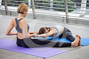 yoga teacher helping young fitness woman doing konasana or wide angle seated forward bend pose Pulling arms and spread leg. in