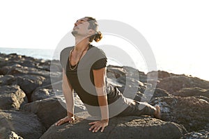 Yoga teacher is practicing on the rocks, sunset time. Man exercising, stretching body. Pranayama. Mindfulness. Meditation