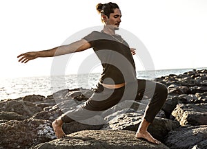 Yoga teacher is practicing on the rocks, sunset time. Man exercising, stretching body. Pranayama. Mindfulness. Meditation