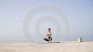 Yoga training by adult woman on empty dock with sea and sky on background